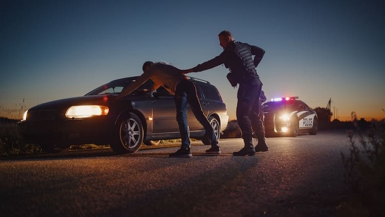 A Professional Middle Aged Policeman Performing a Pat-Down Search on a Fellon With his Hands on Car Hood.